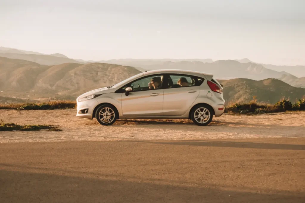 A reliable economy rental car parked safely along the scenic Llogara Pass coastal highway overlooking the Albanian Riviera.